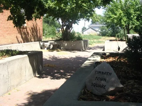 The Timnath Town Square pocket park in Old Town, a brick path between planters with the old school beyond